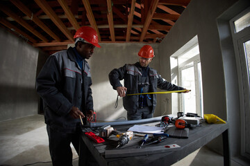 Middle aged Black man and middle aged Caucasian man wearing hard hats working together on...