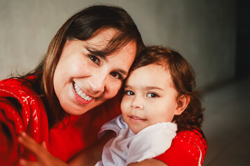 Latin mother and child having fun during Christmas time. Mom and toddler daughter taking self picture together