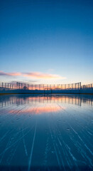 Serene ice skating rink reflecting sunset colors under clear sky  