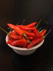 Red chilies in a white bowl with a yellow tomato. Red chilies (Capsicum annuum) fill a white ceramic bowl. The chilies are vibrant with green stems, spilling out to the sides of the bowl