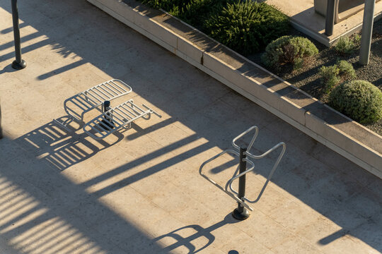 A top-down view of metal outdoor fitness equipment casting long parallel shadows on a light stone surface. Modern landscaping and clean symmetry create a minimalist urban aesthetic - Powered by Adobe