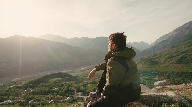 Man sitting on rocky cliff surrounded by spring mountains camera slowly circling around traveler concept of mindfulness freedom sunrise harmony with nature peaceful solitude outdoor inspiration