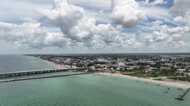 Aerial view of the crowded beach of Progreso, Yucat&aacute;n, showing turquoise water, umbrellas, and the city under dramatic clouds.