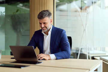 Fototapeta premium Professional Man in Blue Suit Working On Laptop At Modern Office Desk