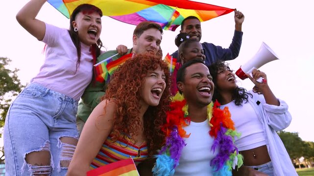 Diverse group of young people celebrating gay pride day outdoors with a rainbow flag and a megaphone, happily shouting together in support of human rights for the lgbtqia plus community