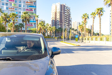 Driver inside car on city street, urban road, traffic sign, modern buildings, transportation concept.