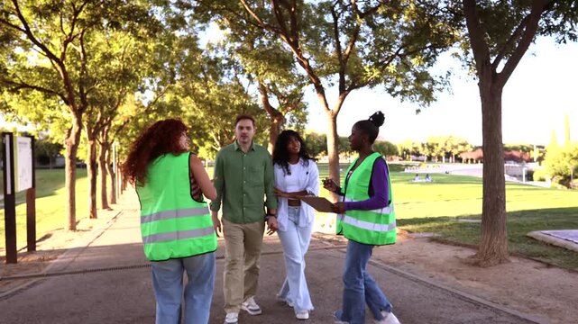 Two dedicated female activists wearing green vests asking people to sign a petition on a clipboard to support their cause, successfully getting signatures from a couple walking in a public park