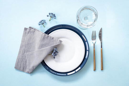 Festive table setting with empty plate and glass, cutlery and napkin - blueberries decorated, flat lay. Top view