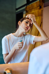 Young woman applies a cosmetic serum to her forehead with a dropper in front of a mirror, performing a morning routine