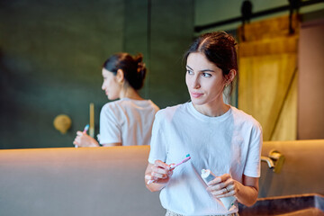 Woman holding a toothbrush and toothpaste, preparing to brush teeth in her modern bathroom, focused on daily dental care