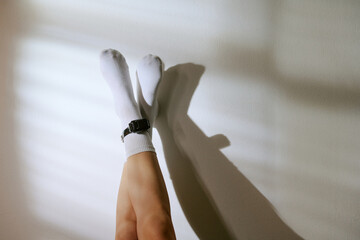 Legs of woman lying on floor with legs crossed wearing electronic ankle monitor, sunlight casting...