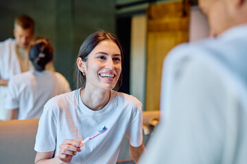 Smiling woman holding a toothbrush with toothpaste, looking at her partner in the morning bathroom routine, promoting hygiene and togetherness