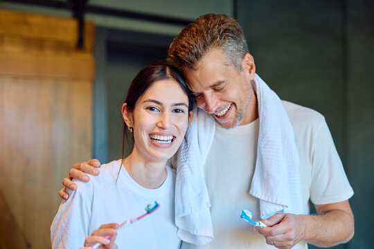 Smiling couple sharing a cheerful morning routine while brushing their teeth in the bathroom, showing dental hygiene and wellness - Powered by Adobe