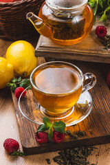Tea in a glass mug on the table next to mint, raspberries and fruits