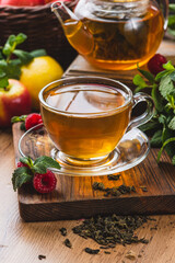 Tea in a glass mug on the table next to mint, raspberries and fruits