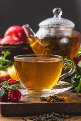 Tea in a glass mug on the table next to mint, raspberries and fruits
