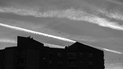 silhouette of apartment building under dramatic sky with contrails in black and white