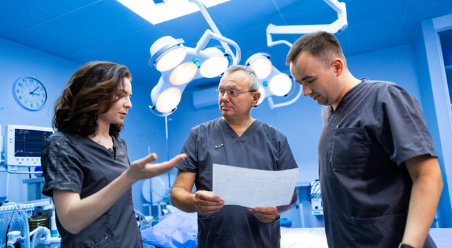 Surgeons analyzing patient report. Medical staff examining document in bright surgery room