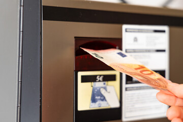 Funchal, Portugal - November 11, 2025: Hand inserting ten euro banknote into payment machine for...