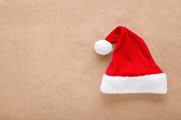 Bright red hat with white fur on dry sea sand background. Closeup. Garment for Christmas...