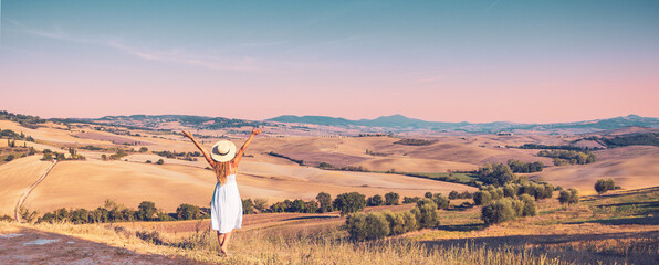 Happy girl in white dress and hat enjoying field in Italian Tuscany at sunset