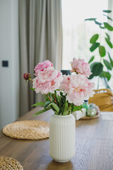 Soft pink peony flowers in a white ribbed vase on a wooden table in a bright modern home interior © Anna Lurye