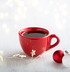 Red cup of coffee, Christmas decorations and lights of garland   on white  rustic wooden  table. Selective focus.