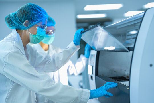 A team of pathologists processes samples using an automated staining machine. They are conducting pharmaceutical research or diagnostic testing in a sterile biotech lab.