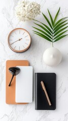 A minimalist desk setup featuring a rose gold clock, notebooks, pen, and a green leaf on a marble surface.