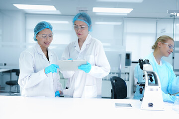 A pharmaceutical Quality Control QC team ensures GxP compliance. Two scientists review an electronic batch record on a tablet while a third performs a required analytical test.