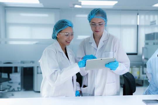 A senior scientist mentors a junior colleague in a modern lab, using a tablet to guide her through a precise pipetting technique, fostering hands-on learning and skill development. - Powered by Adobe
