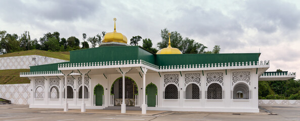 Royal Mausoleum, Kubah Makam Diraja, Bandar Seri Begawan, Brunei Darussalam. White building with green roof, golden domes, and intricate Islamic patterns.