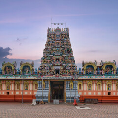 Vibrant Kandaswamy Kovil Hindu temple in Kuala Lumpur, Malaysia, featuring an intricately carved gopuram with colorful deities against a soft twilight sky.