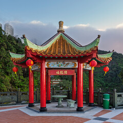 Obraz premium Vibrant red Chinese blessing pavilion with ornate green and orange roof, red lanterns, and stone seating at Chin Swee Caves Temple complex, Genting Highlands, Malaysia