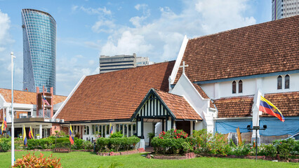 Historic St. Mary's Cathedral, an Anglican church with traditional architecture and red tiled roof, contrasting with a modern skyscraper under blue sky in Kuala Lumpur, Malaysia