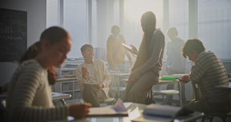 Teens Chatting and Fooling Around During Break in Classroom. Girl Starts Filming Guy on Phone. Boy Laughs and Hides Behind Some Papers. Concept Leisure Time During Break, Reflecting Youth Culture. - Powered by Adobe