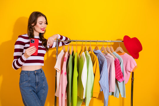 Young woman shopping for colorful clothes on a rack against a bright yellow background for fashion lifestyle and style