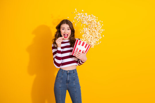 Young girl with striped top holds popcorn bucket smiling yellow background in playful fashion promoting shopping lifestyle fun moments