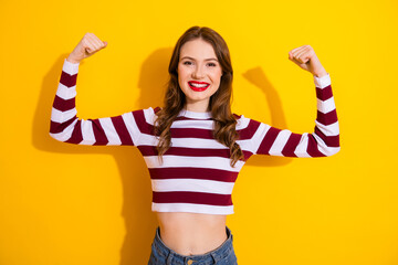 Young woman in striped crop top flexing arms against bright yellow background for fashion lifestyle...