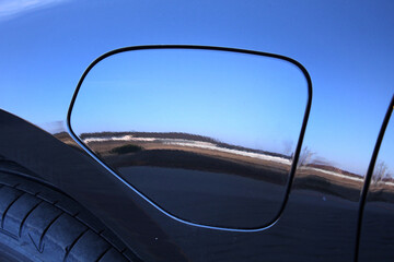 Sleek fuel filler door on lux sedan painted in metallic black. Fuel door softly rounded corners. Featuring chrome car trim and premium build quality. Car fuel door. Electric vehicle charging hatch.