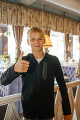 Boy gives thumbs up inside modern cafe