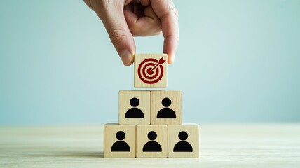 A hand places a target block on a stack of blocks representing people, symbolizing goal-setting and strategic planning in business.