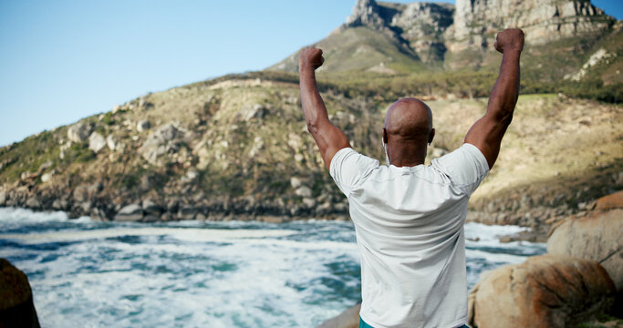 Runner, beach and celebration with black man for fitness goal, success or win at sea. Back, sports achievement and mature athlete by ocean for workout target, health and earphones for music outdoor - Powered by Adobe