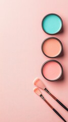 Three open containers with colored creams and two brushes on a pink textured surface.