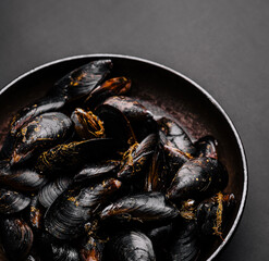 Freshly cooked mussels served in a dark bowl on a simple background