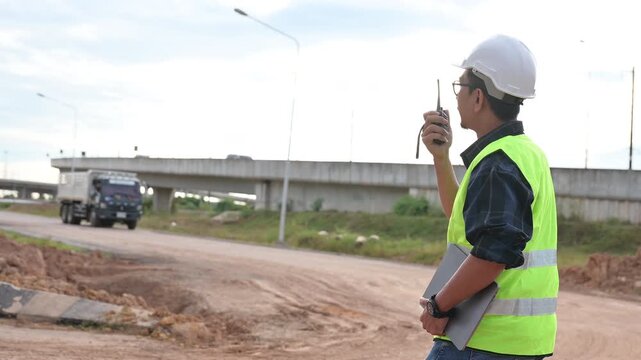 Coordination of Construction Foremen A construction foreman oversees operations on a construction site while donning a hardhat, safety vest, and radio.