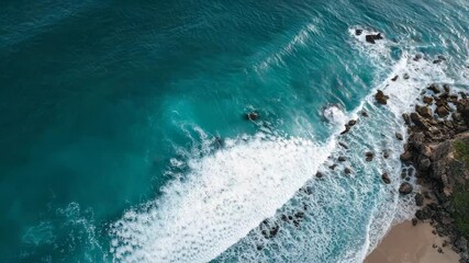 Aerial drone view of turquoise ocean waves crashing on rocky shore and sandy beach with white foam and - Powered by Adobe