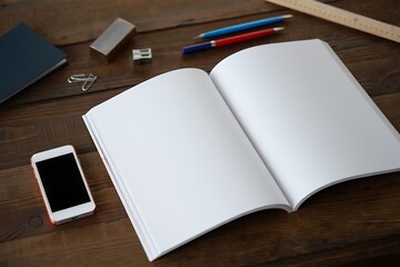 Open blank book with smartphone and writing tools on wooden desk