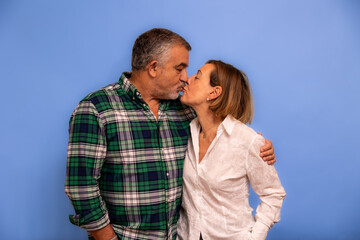 Fototapeta premium Elderly couple sharing loving kiss on blue background