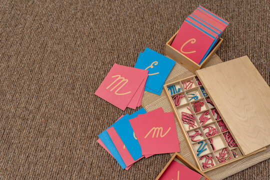 Montessori written sensory materials. Pink and blue letter cards and cut out letters in a wooden tray. Develops muscle memory, understanding of shape and hand movements in elementary school.